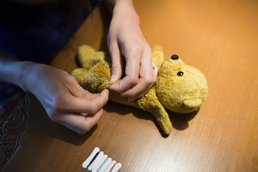 man sewing back together his stuffed teddy bear