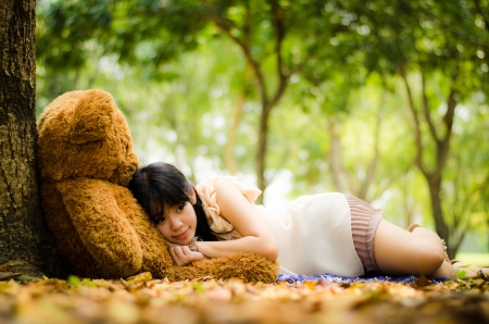 girl resting under a tree with a teddy bear