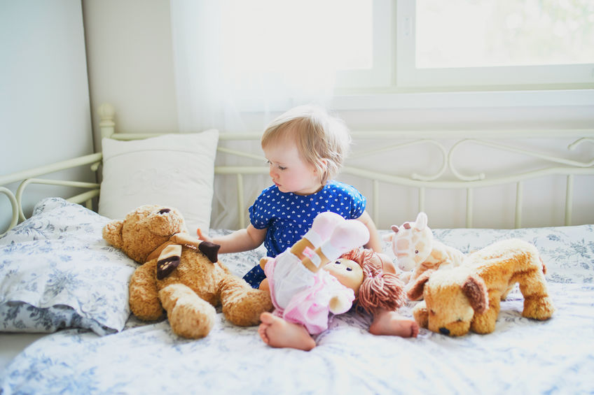 young girl sitting on bed with stuffed animals