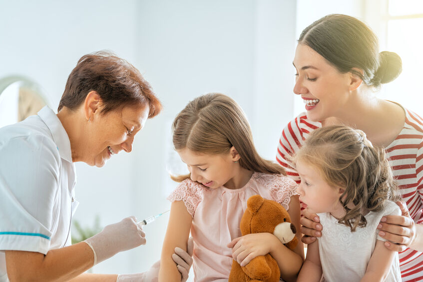 child receiving vaccine from doctor with family beside her