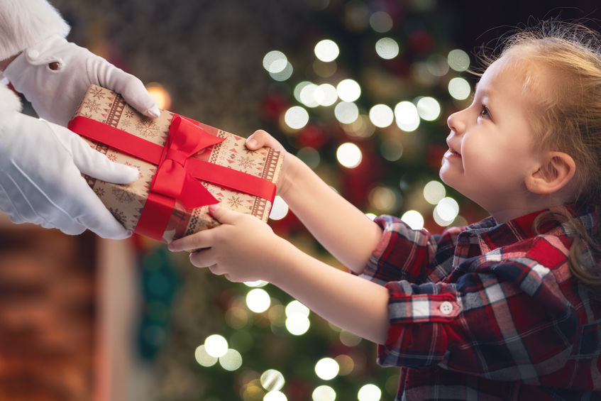 adult handing christmas present to young girl