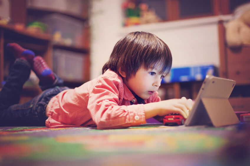 toddler lying on floor staring at tablet screen