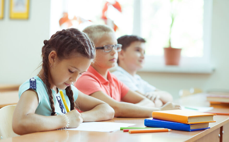 Happy schoolchildren studing and answer questions in classroom during a lesson at primary school