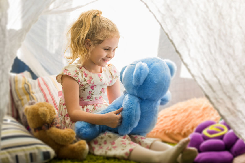 Little blonde child girl playing at home in her room with teddy bears.